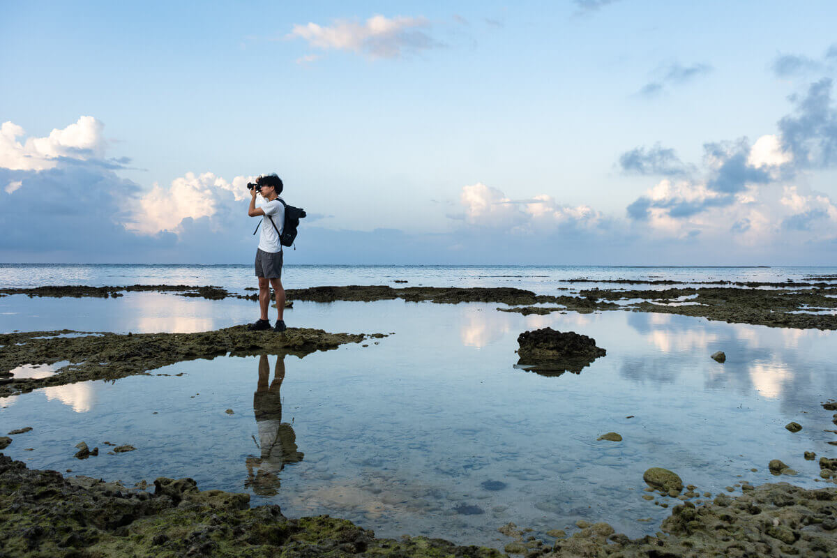 浅瀬の海岸でカメラを構えて立つ人