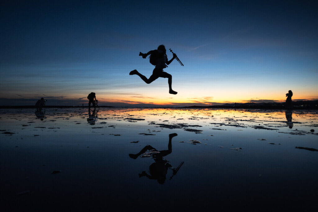 夕暮れ時の浅瀬の海岸でジャンプする人