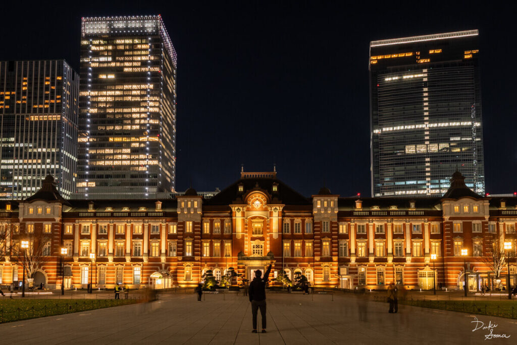 夜の東京駅の前でポーズをとる人