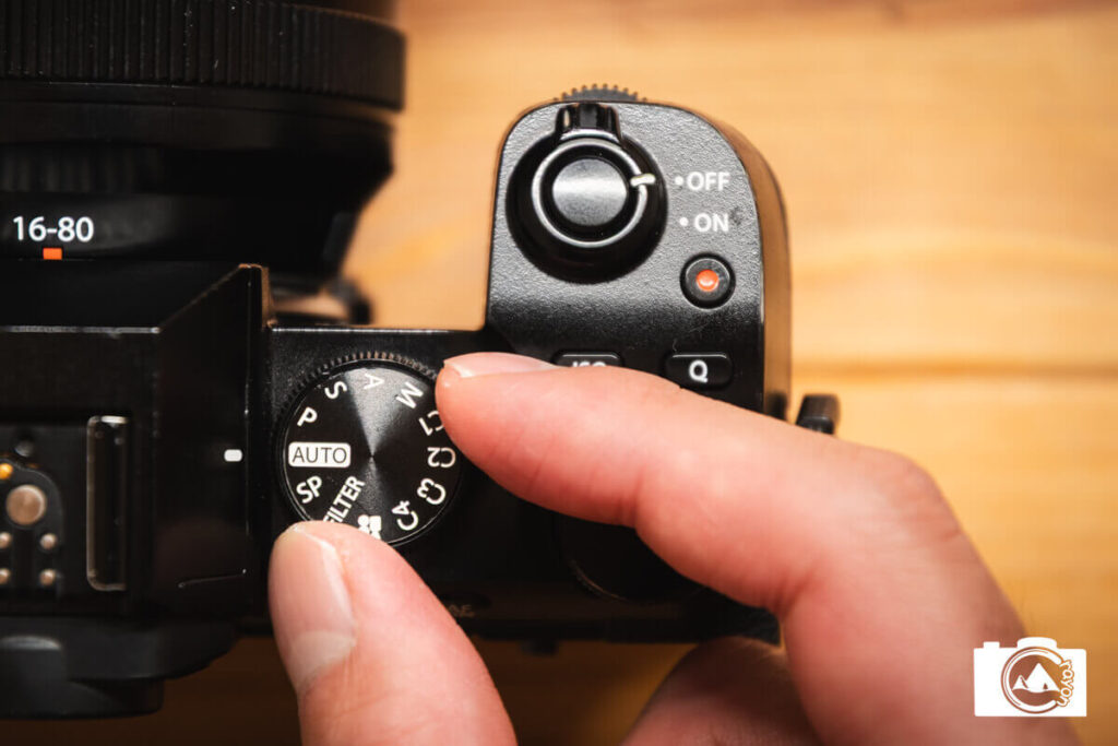 カメラの撮影モードダイヤルを回す手