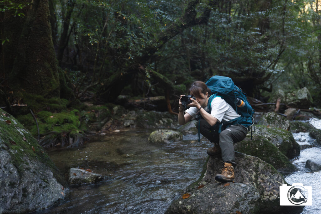川でしゃがんで写真を撮る女性