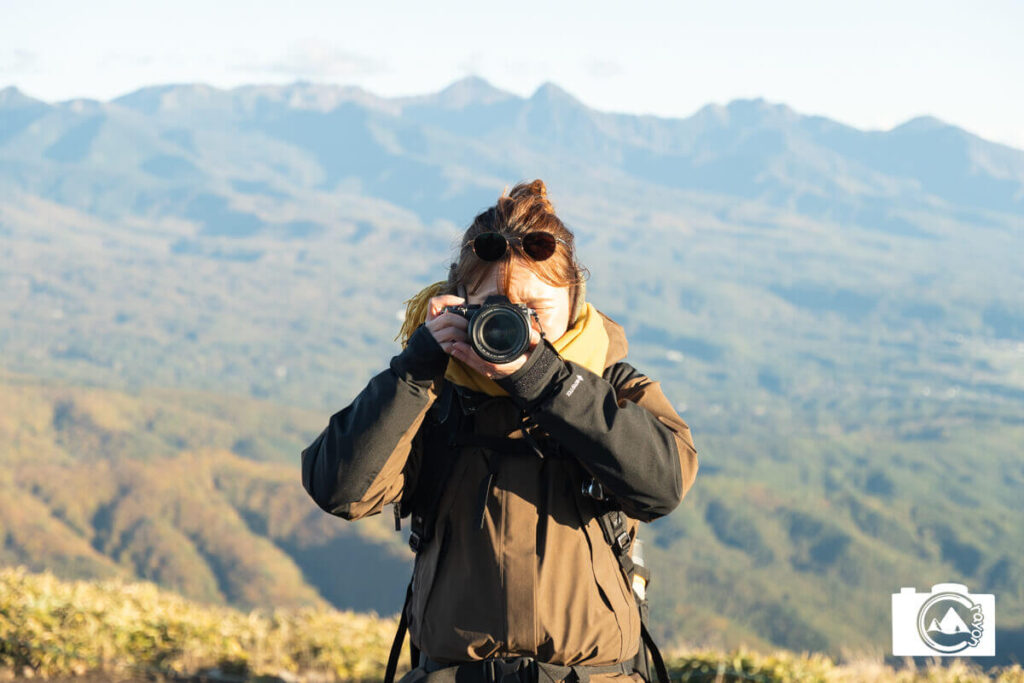 山を背景にカメラを構える女性