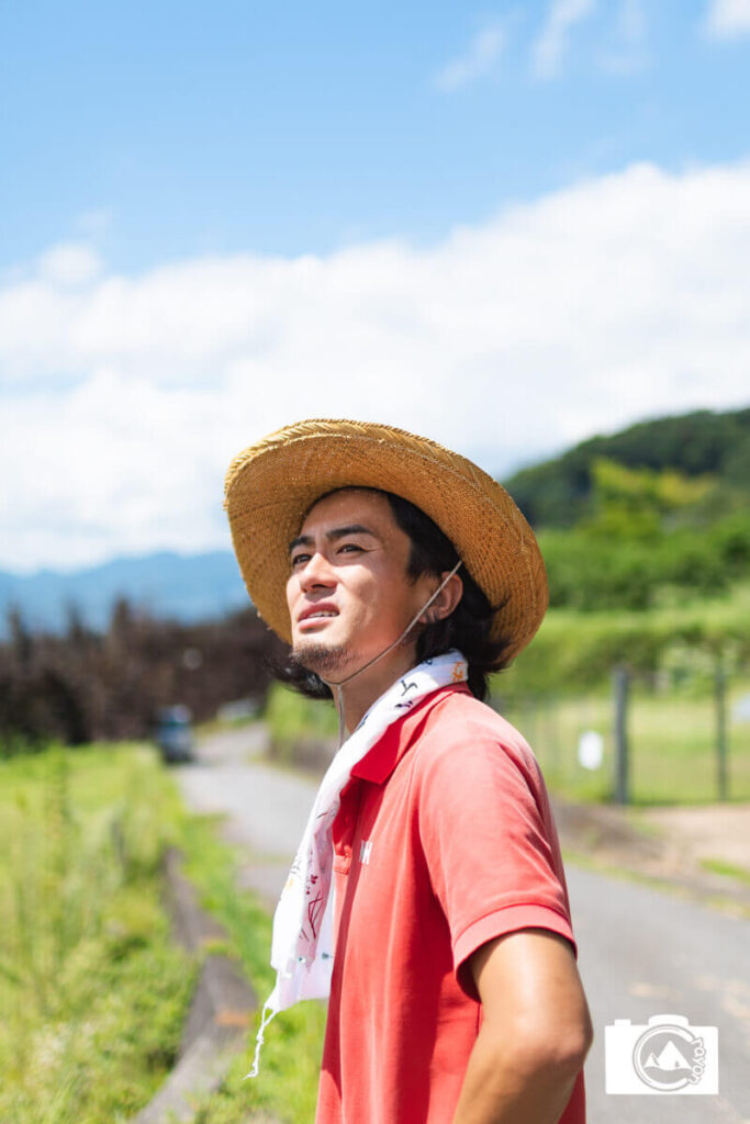 夏の田舎道でポーズをとる麦わら帽子の男性