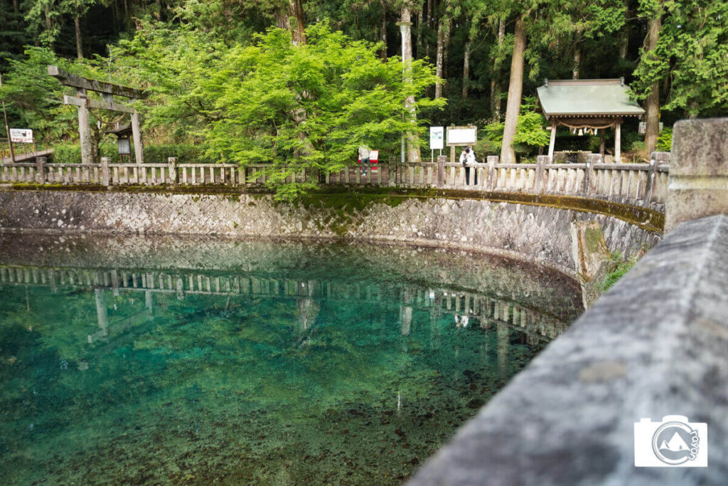 青く透き通った池と、それを眺める女性